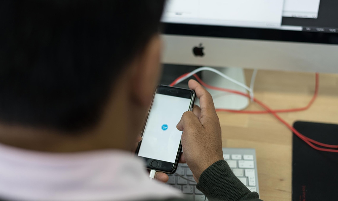 A man using a cell phone in front of a computer.