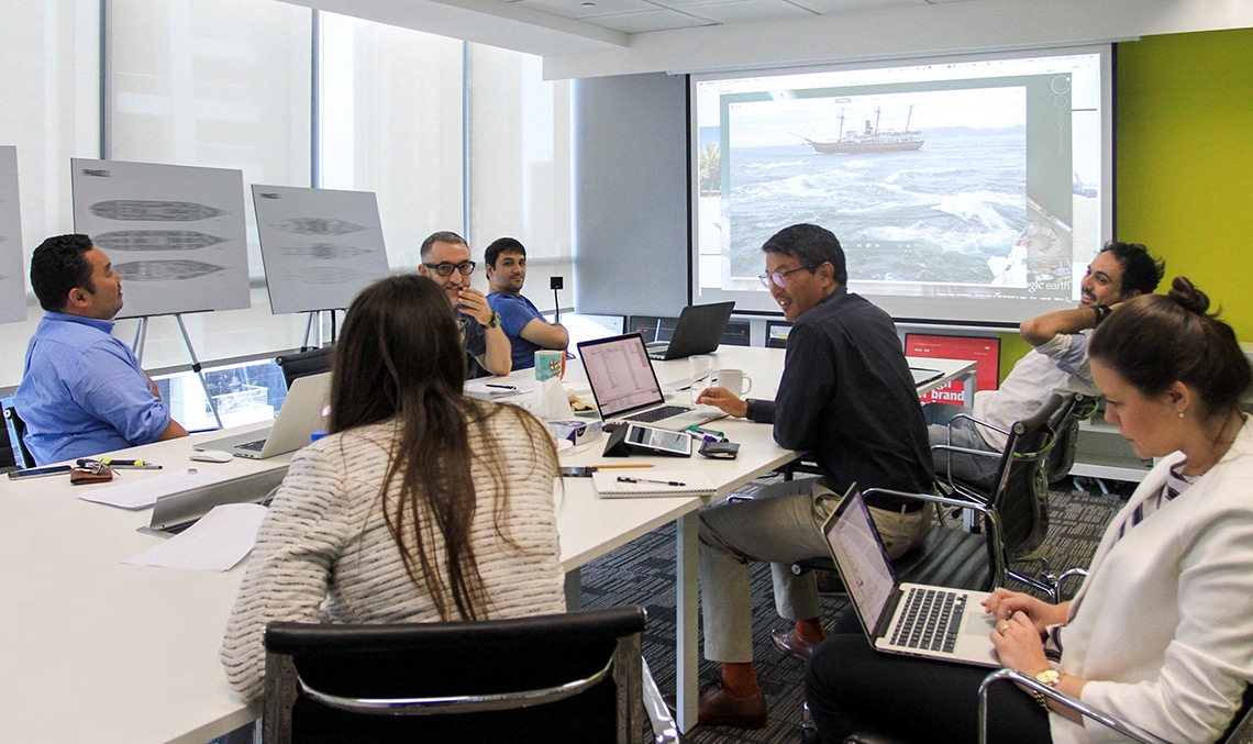 A group of people sitting around a table with laptops.
