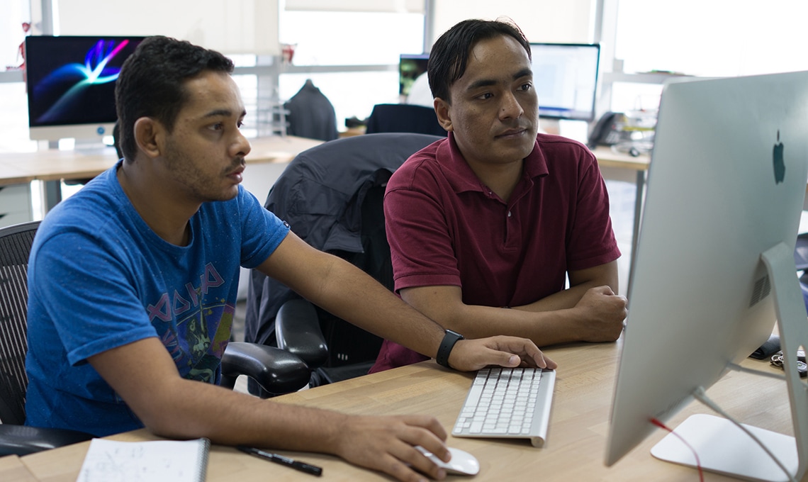 Two men sitting at a desk looking at a computer.