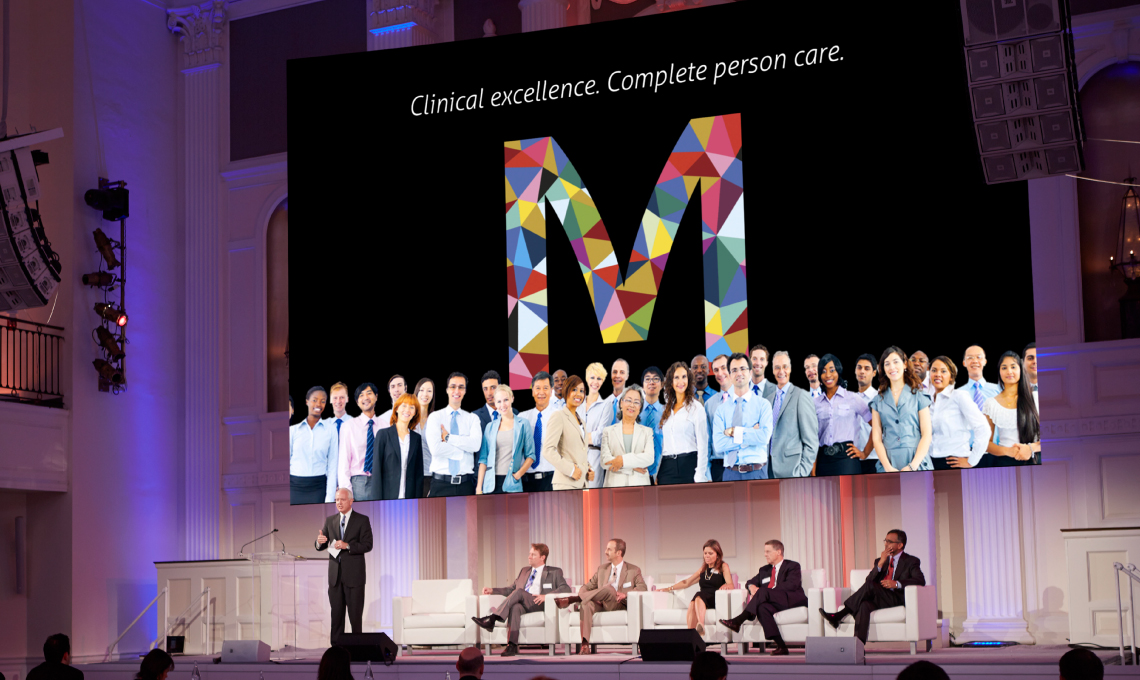 a group of people sitting on a stage in front of a large screen.