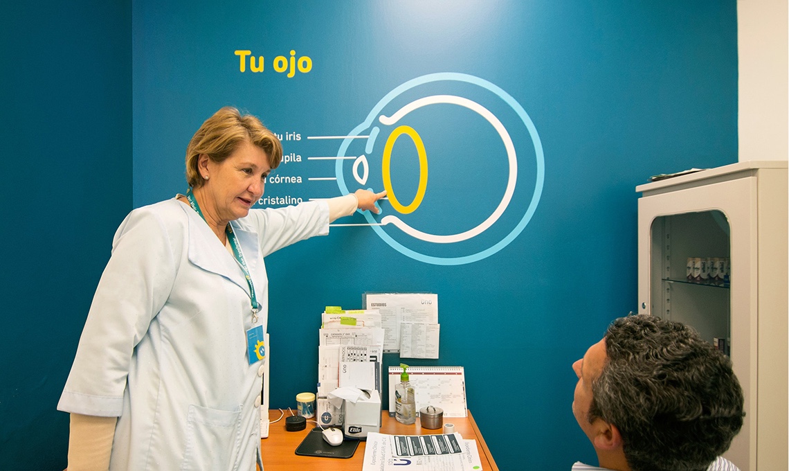 A woman in a lab coat is redefining the experience of seeing by pointing to a diagram on a wall.