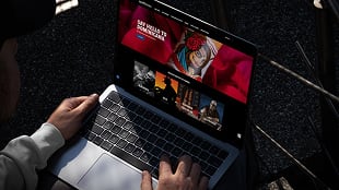 Person using a laptop outdoors, displaying a website with various images and brightly colored graphics on the screen.